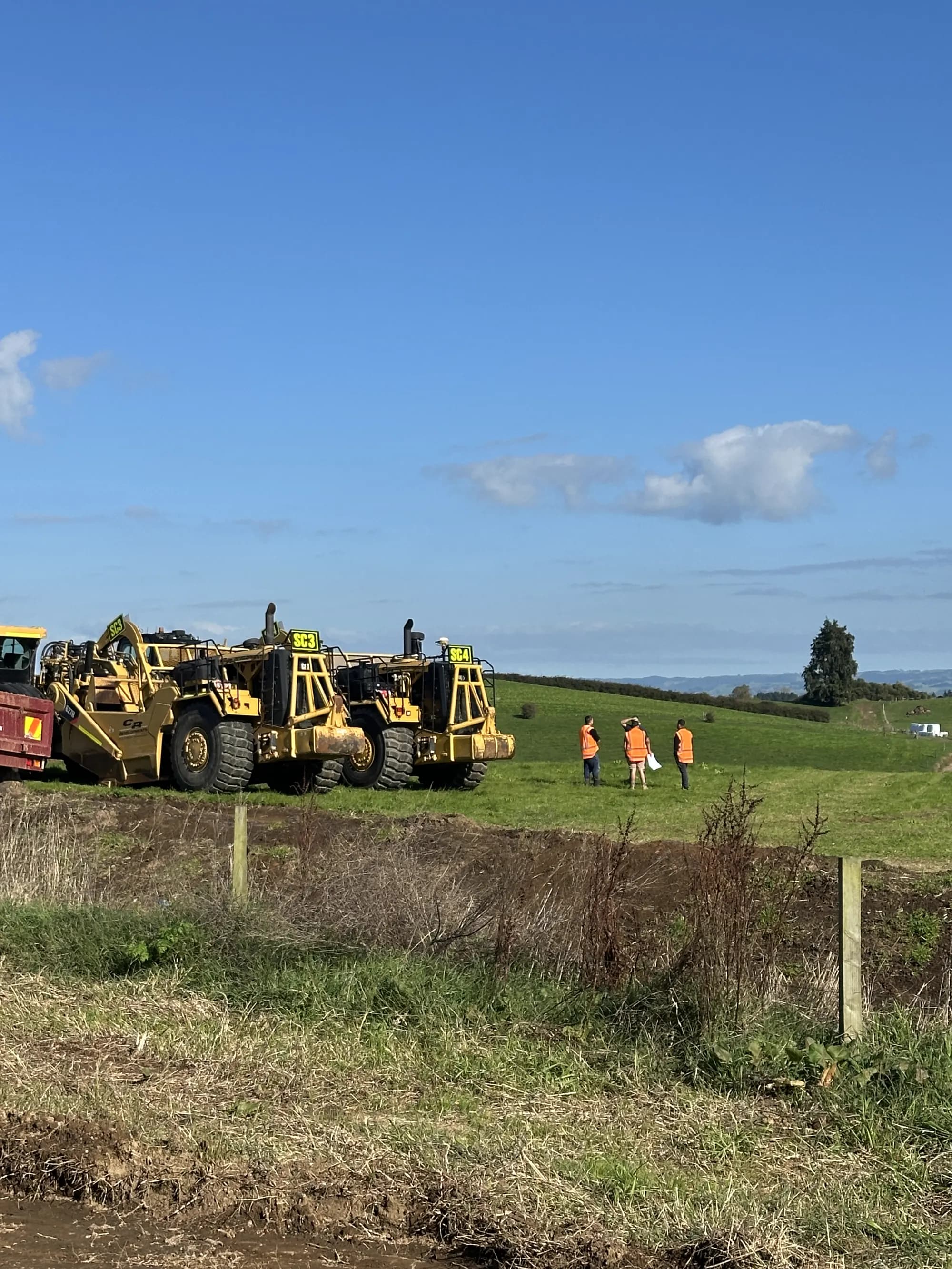 Earthmoving scrapers parked on open farmland at the Parkview site, with surveyors standing on the rise beyond